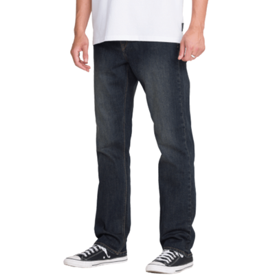 man in a white volcom logo t-shirt wearing dark blue volcom solver denim jeans with black converse all stars on a white background
