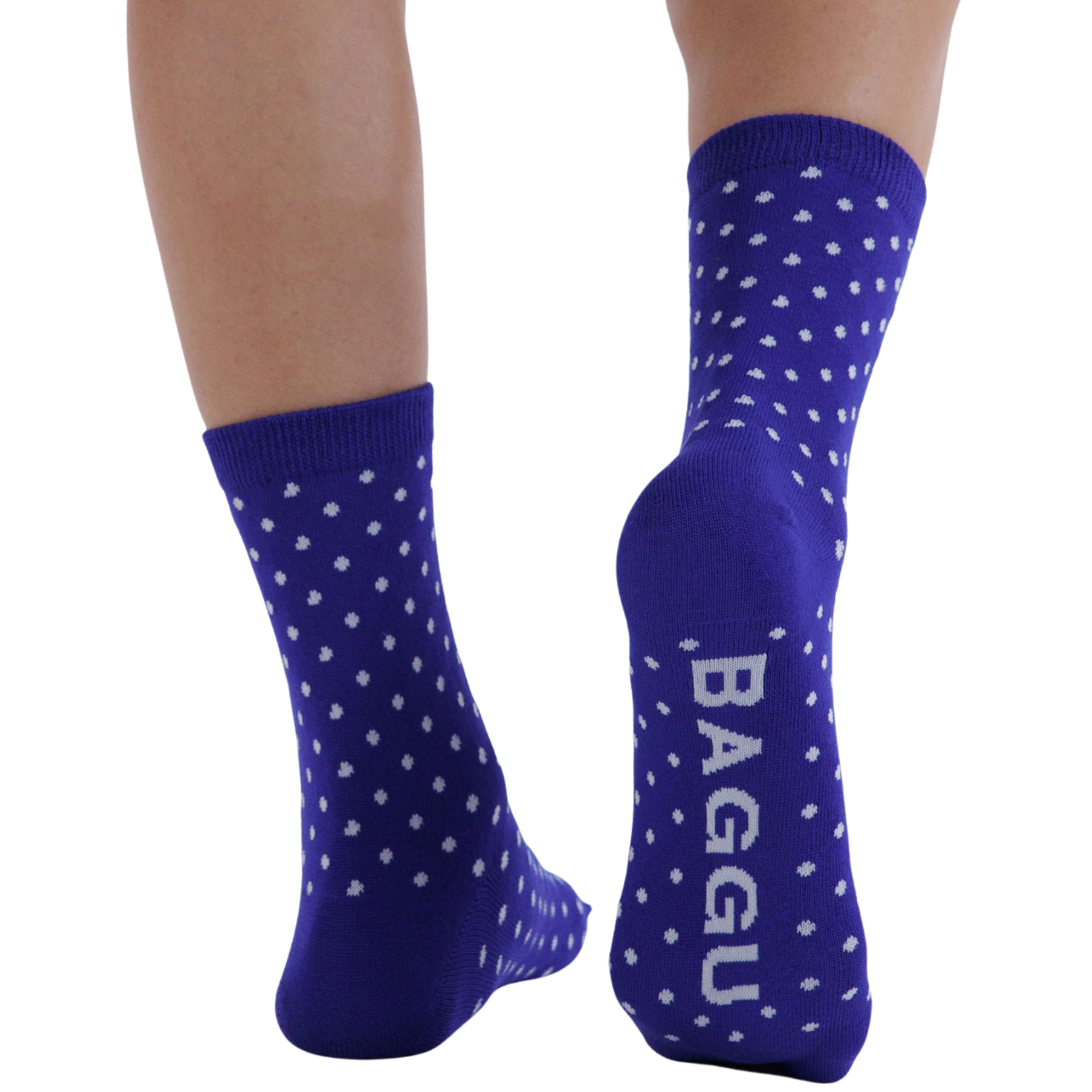 A pair of royal blue baggue crew socks with white polka dots and the brand name 'BAGGU' printed vertically in white on the sole, shown on a person's feet against a white background.