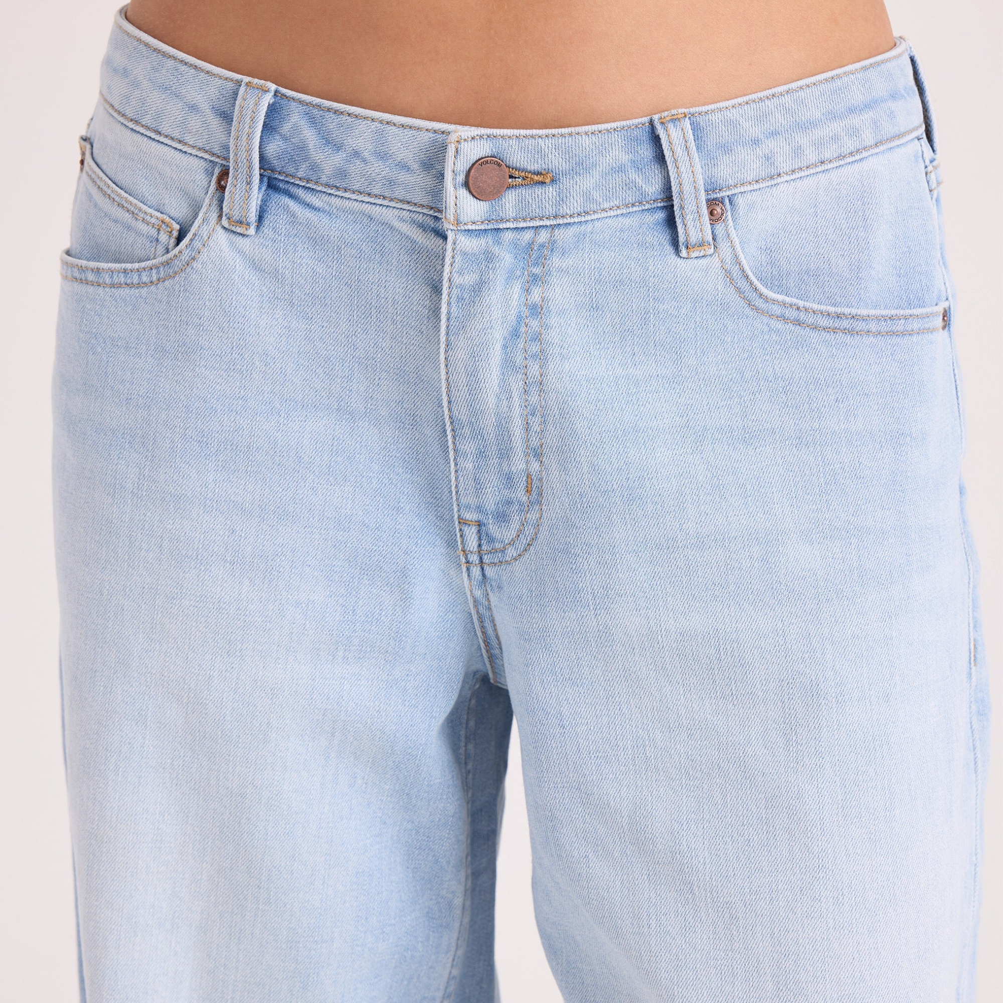 A woman in a black hat and black tee shirt wearing volcom stoned boyfriend low rise jeans on a white background