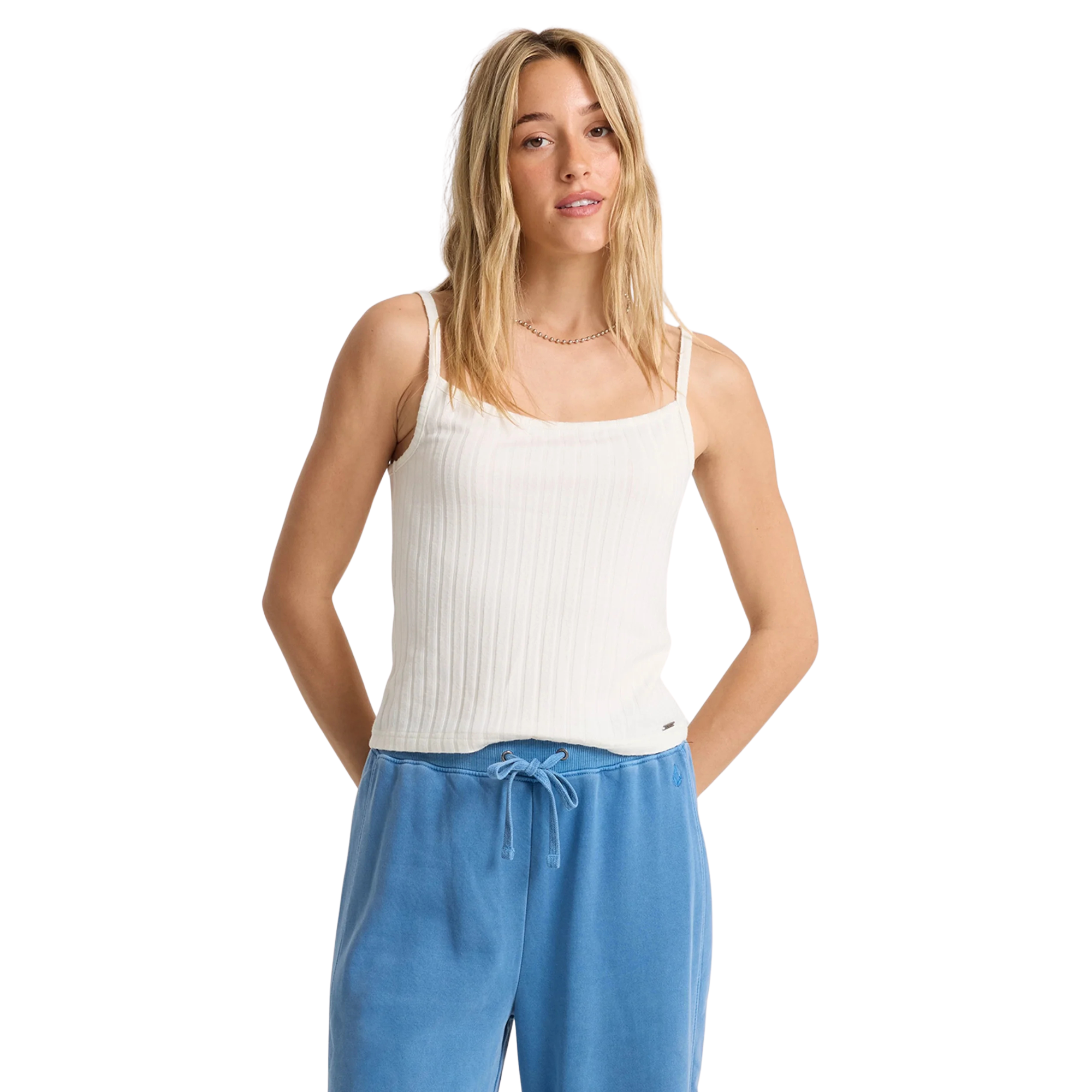 Woman wearing a volcom lived in rib white tank top and blue pants on a white background