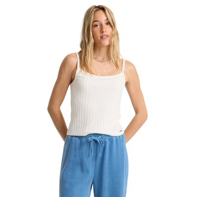Woman wearing a volcom lived in rib white tank top and blue pants on a white background