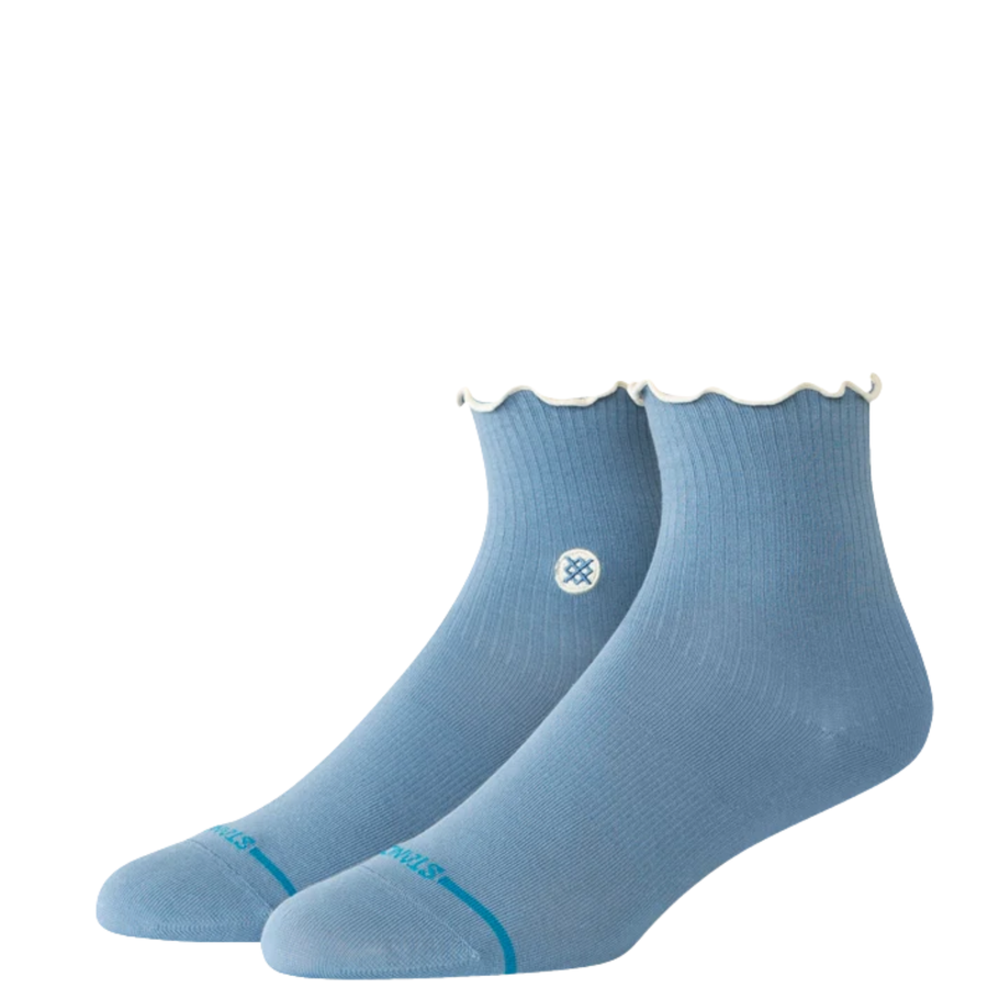 A pair of stance light blue ankle socks with scalloped ruffle edges at the top and a small white circular logo on the side, displayed against a plain white background.
