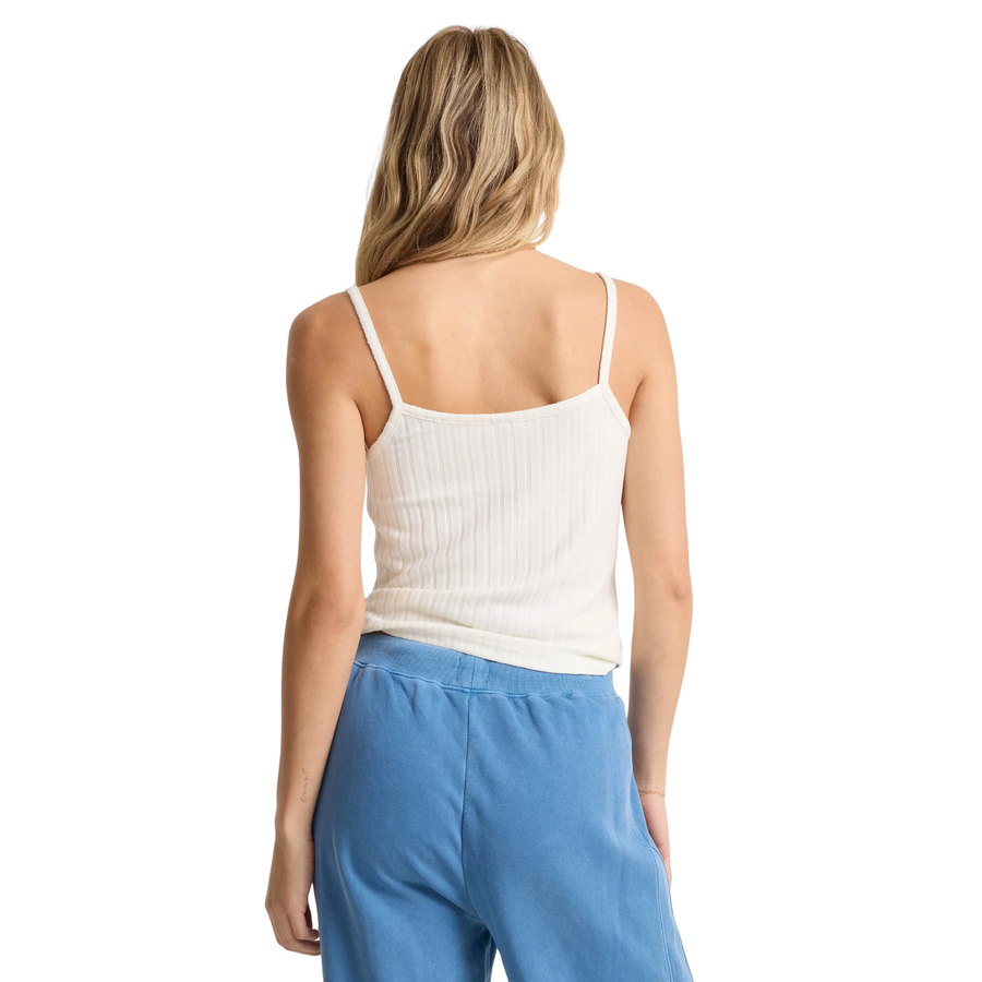 Woman wearing a volcom lived in rib white tank top and blue pants on a white background