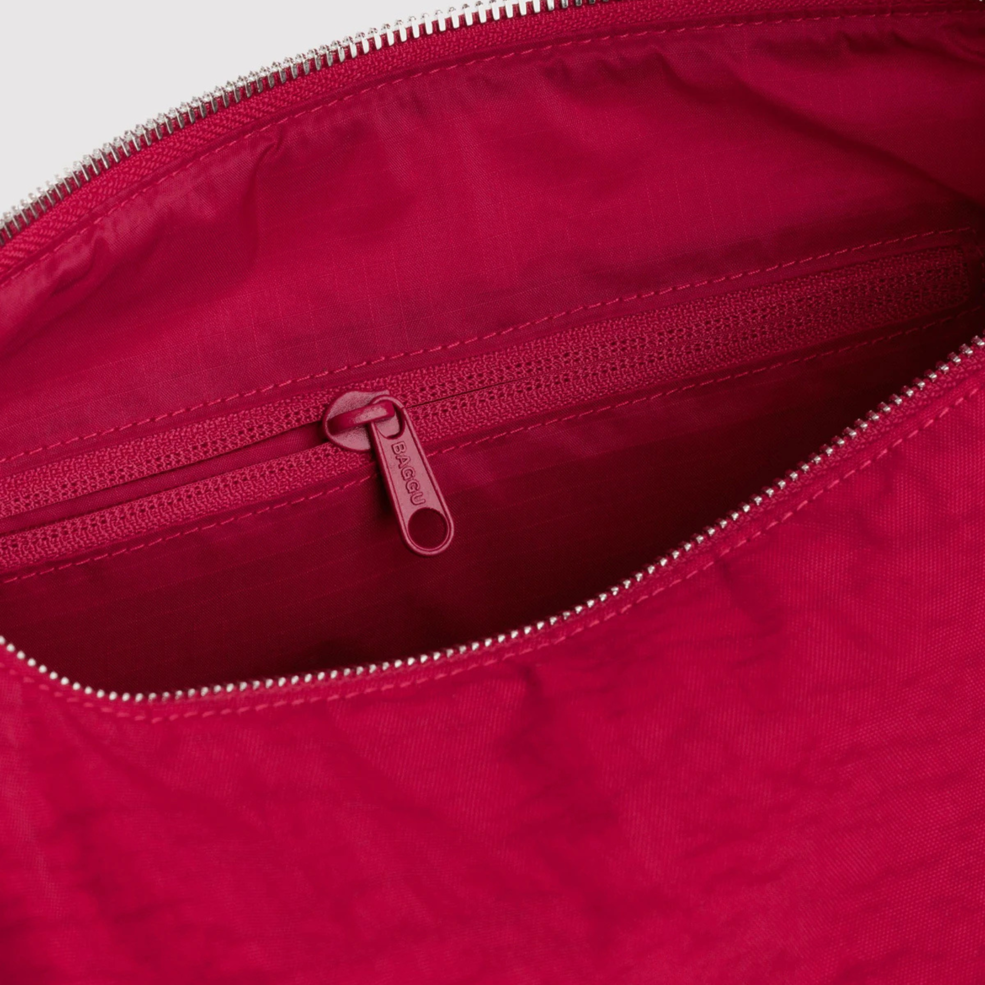 Close-up of the interior of A bright red fabric baggu merigue shoulder bag with a single long strap, shown against a plain white background.