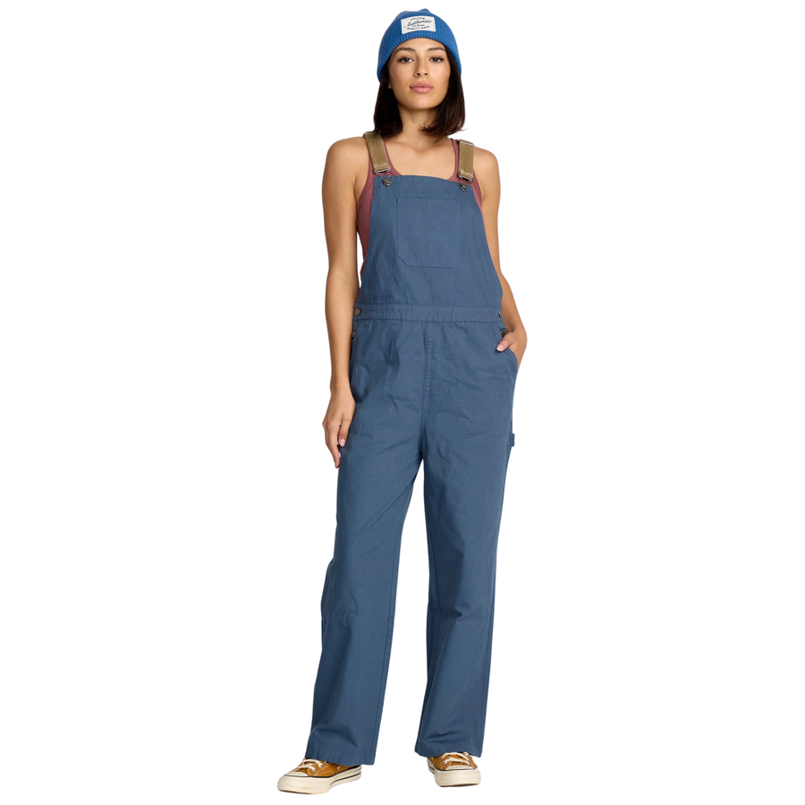 Woman wearing blue volcom full cut overalls with brown cordoroy straps and a matching beanie on a white background