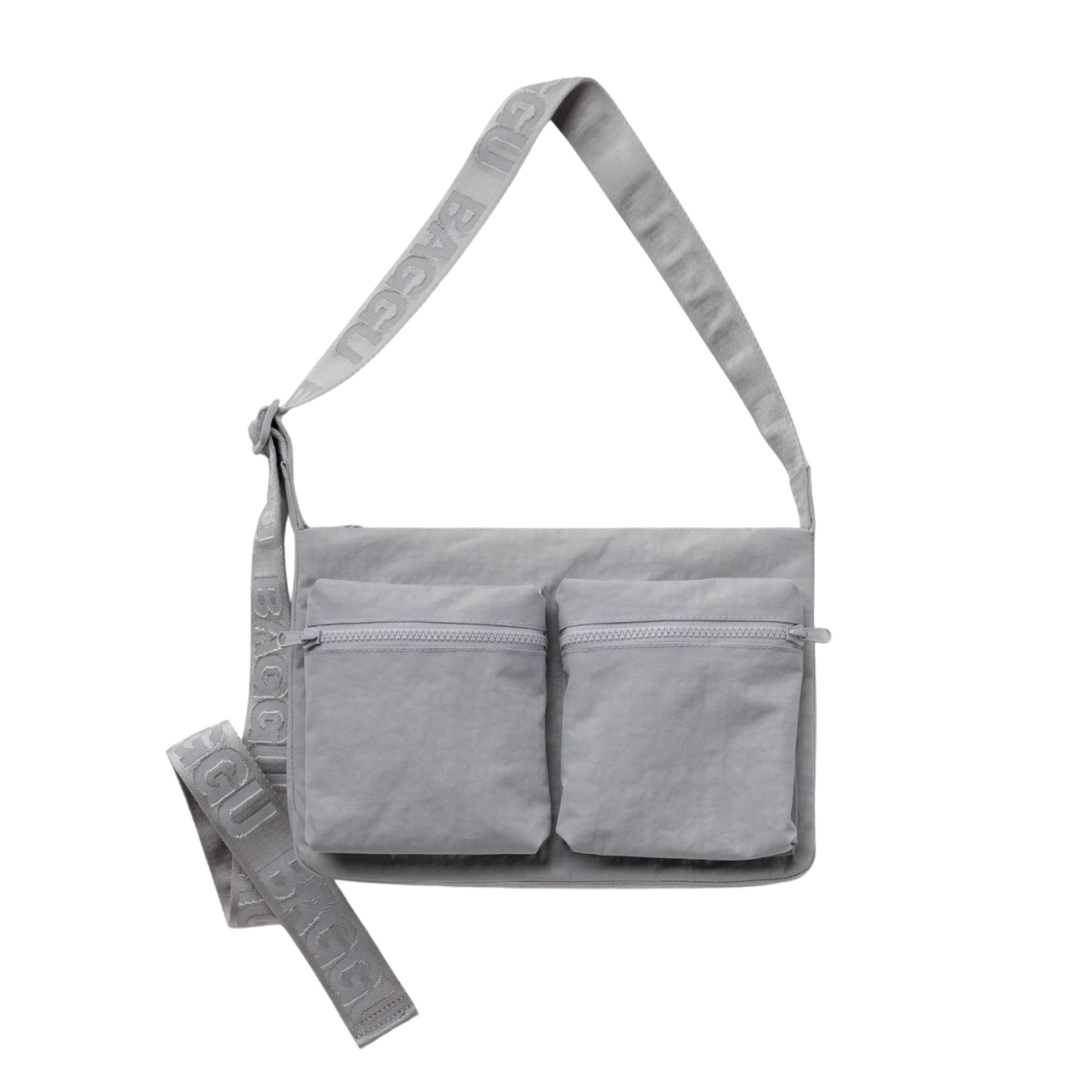 A light gray fabric baggu cargo crossbody shoulder bag with two front zippered pockets and a wide adjustable strap featuring embossed text, shown on a plain white background.