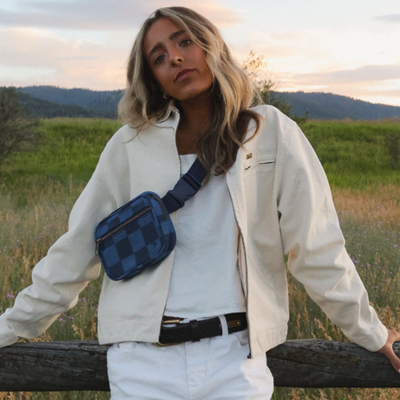 girl in white wearing a blue and navy checkerboard thread belt bag fanny pack in the country