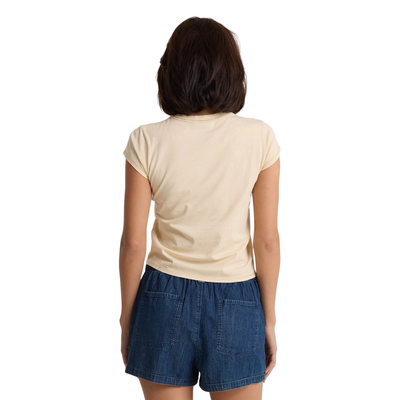 Woman wearing a beige volcom lived in stone wash t-shirt and blue shorts on a white background