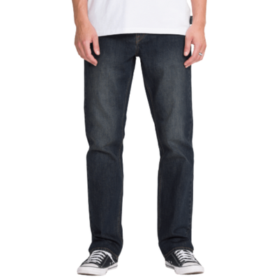 man in a white volcom logo t-shirt wearing dark blue volcom solver denim jeans with black converse all stars on a white background