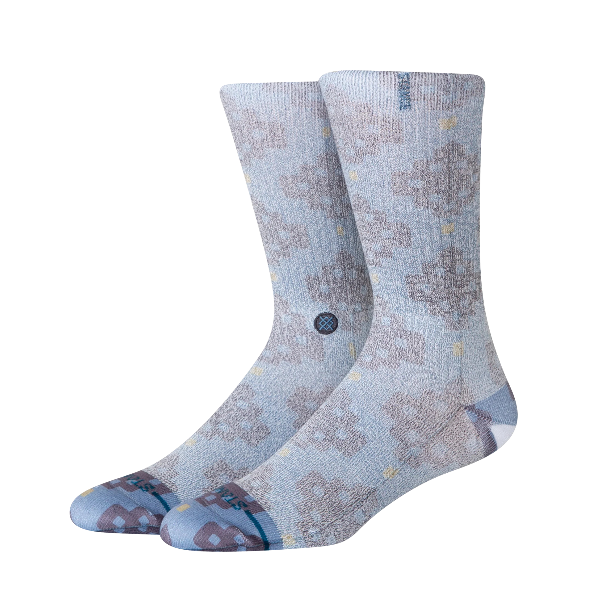 A pair of Stance alhambra butterblend crew socks in a light blue-gray colorway with a distressed brown tree pattern and small yellow accents, shown on a plain white background.