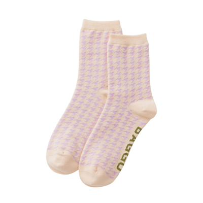 A pair of light pink and lavender houndstooth patterned baggu crew socks with beige ribbed cuffs and toes, featuring the brand name 'BAGGU' printed vertically in olive green on the sole.