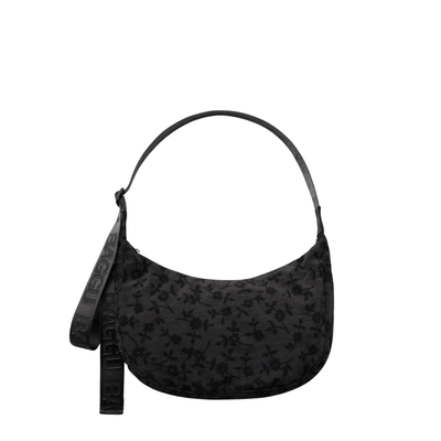 A black crescent-shaped baggu shoulder bag with a subtle tonal floral pattern, featuring a matching black strap with embossed lettering, shown against a plain white background.