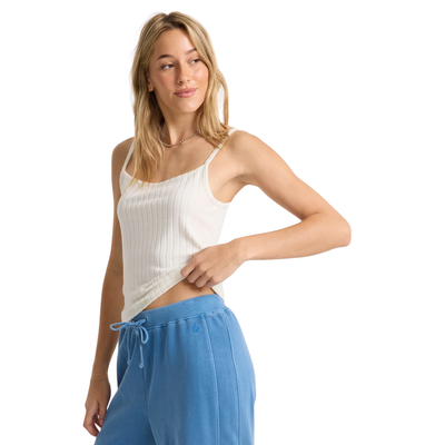 Woman wearing a volcom lived in rib white tank top and blue pants on a white background