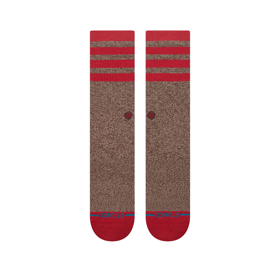 A pair of stance sock monkey crew socks in heathered brown with bright red stripes at the ribbed cuffs, red heels, and red toes, featuring a small red circular logo on the side.
