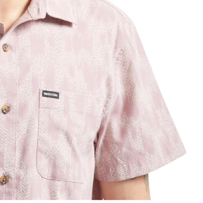 Close-up of s Man wearing a pink brixton charter print patterned short sleeve shirt with brand logo on a white background