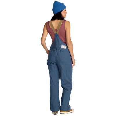 Woman wearing blue volcom full cut overalls with brown cordoroy straps and a matching beanie on a white background