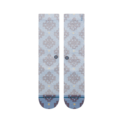 A pair of Stance alhambra butterblend crew socks in a light blue-gray colorway with a distressed brown tree pattern and small yellow accents, shown on a plain white background.