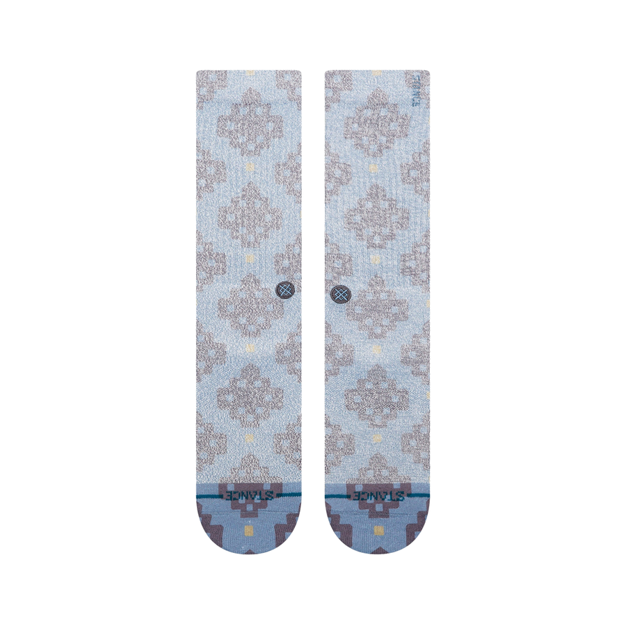 A pair of Stance alhambra butterblend crew socks in a light blue-gray colorway with a distressed brown tree pattern and small yellow accents, shown on a plain white background.
