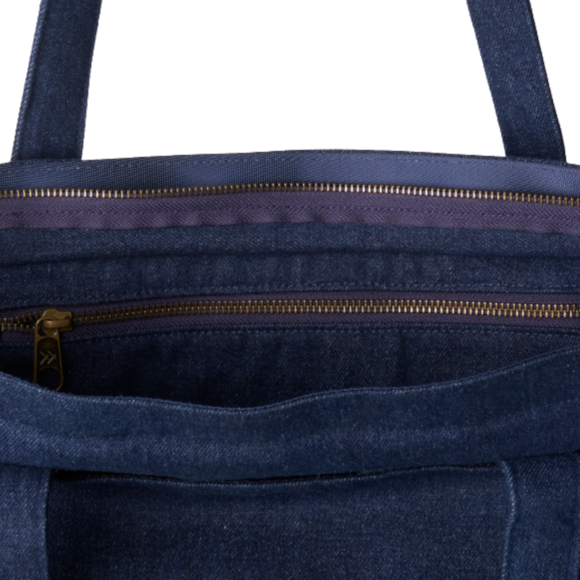 Close-up of the interior of a dark blue denim tote bag, showing two gold-tone zippers and a purple inner lining.