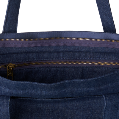 Close-up of the interior of a dark blue denim tote bag, showing two gold-tone zippers and a purple inner lining.