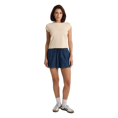Woman wearing a beige volcom lived in stone wash t-shirt and blue shorts on a white background