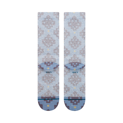 A pair of Stance alhambra butterblend crew socks in a light blue-gray colorway with a distressed brown tree pattern and small yellow accents, shown on a plain white background.