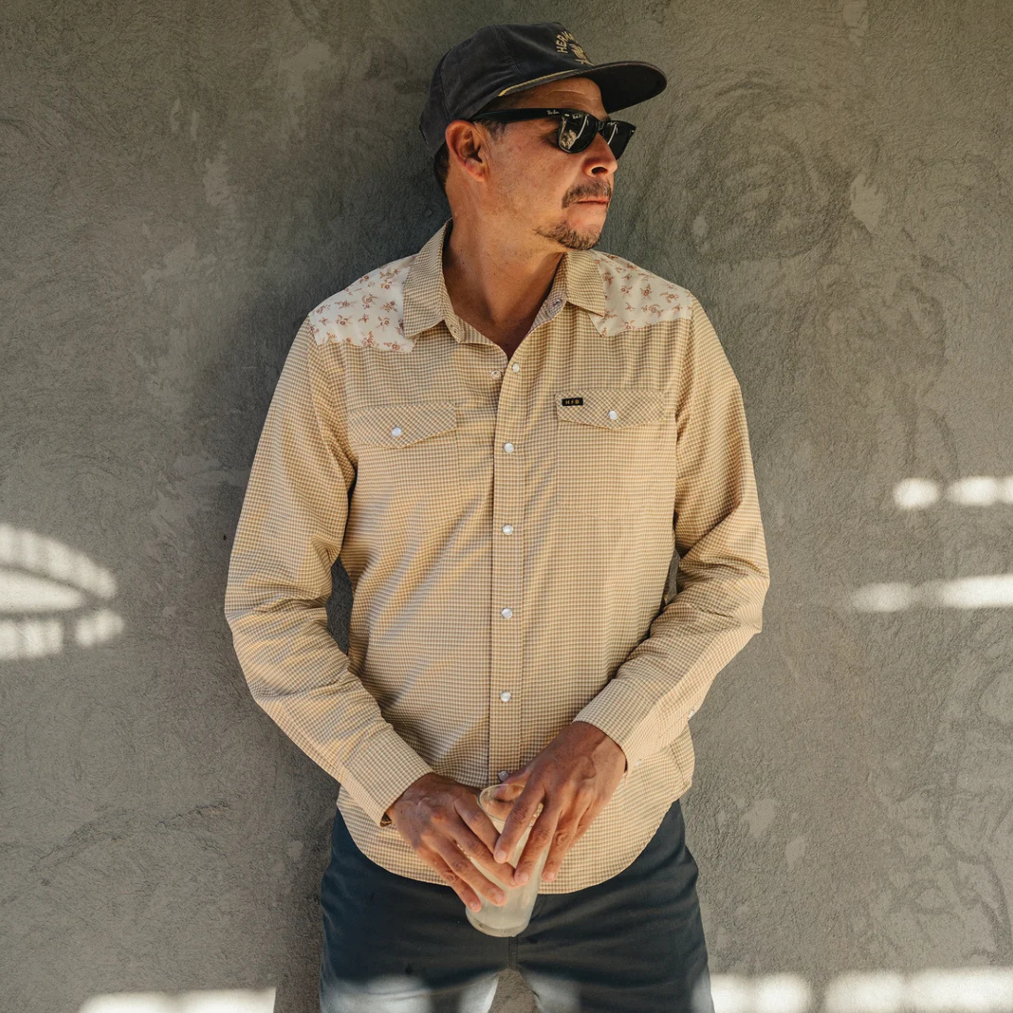 a man wearing A beige and brown checkered long-sleeve howler h bar tech western shirt with beige floral patterned yoke panels on the shoulders, featuring two buttoned chest pockets and a button-down front.