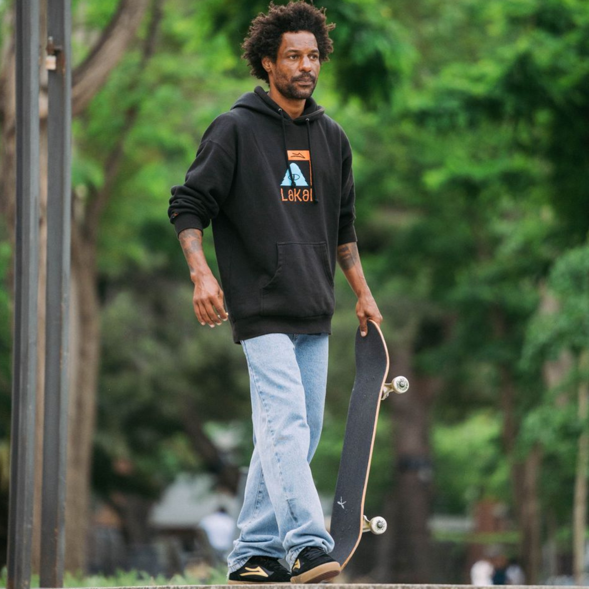 bastian salabanzi holding a skateboard with a blurred green outdoor background