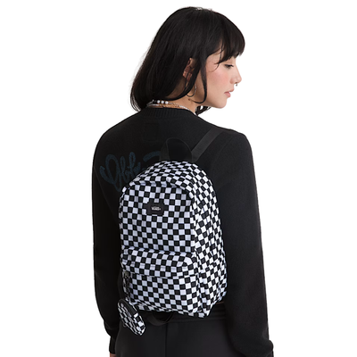 a girl in black wearing a black and white checkerboard mini vans backpack on a white background