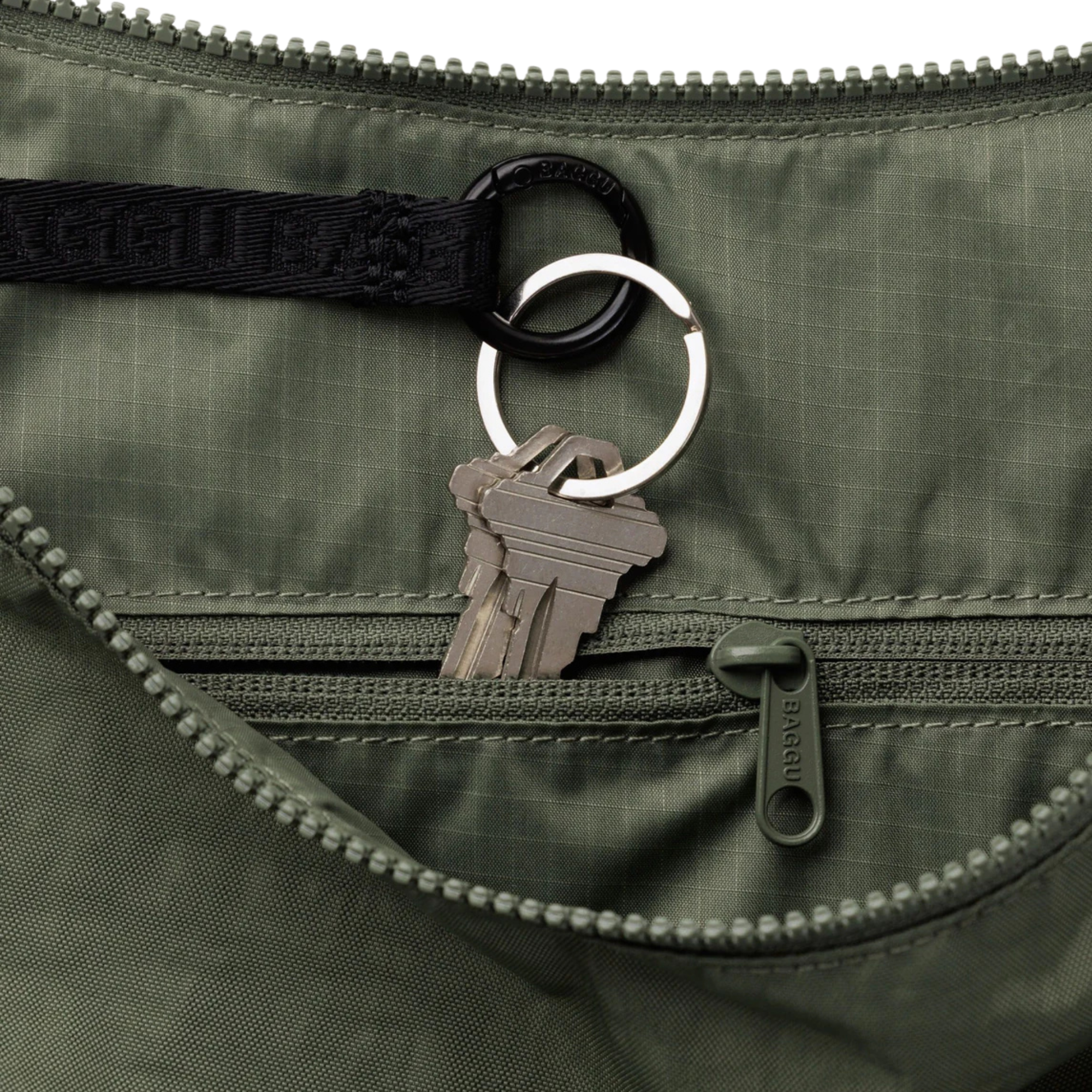 Close-up of an olive green baggu nylon bag with a black webbed strap, silver keyring, and metal keys attached near a zippered pocket.