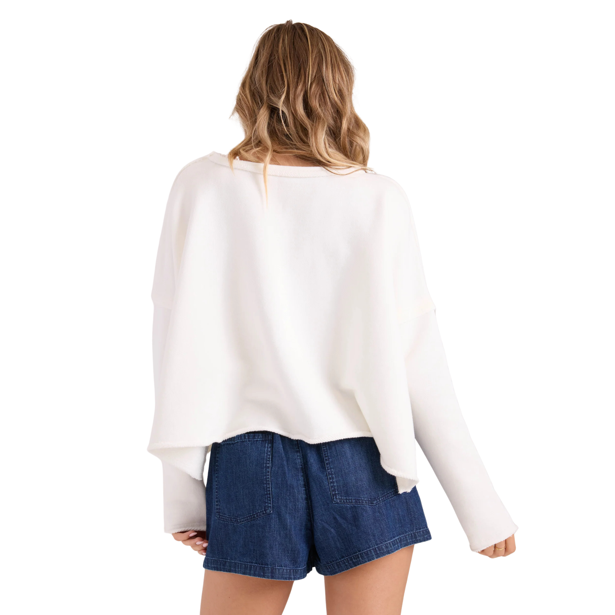 a woman wearing a white volcom gnarly sweatshirt and blue denim shorts on a white background