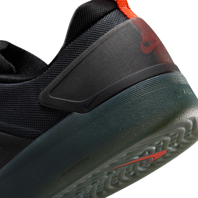 close up of A black Nike nyjah 4 skateboard sneaker with a textured synthetic upper, black laces, a black sole, and a small red pull tab on the heel, shown from a side profile against a white background.