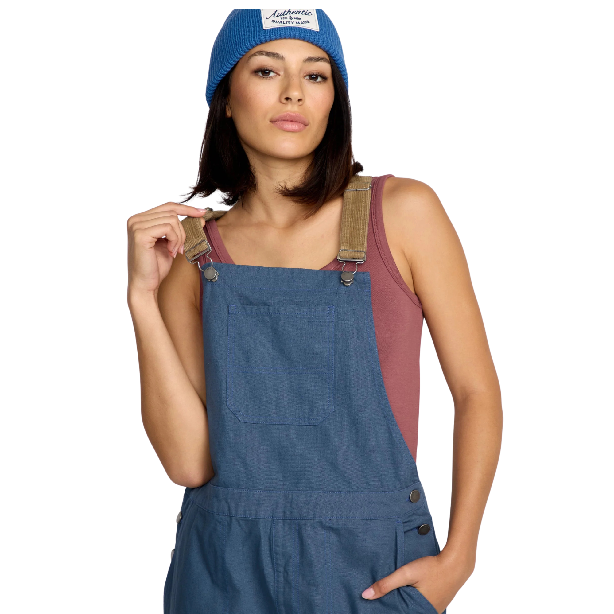Woman wearing blue volcom full cut overalls with brown cordoroy straps and a matching beanie on a white background