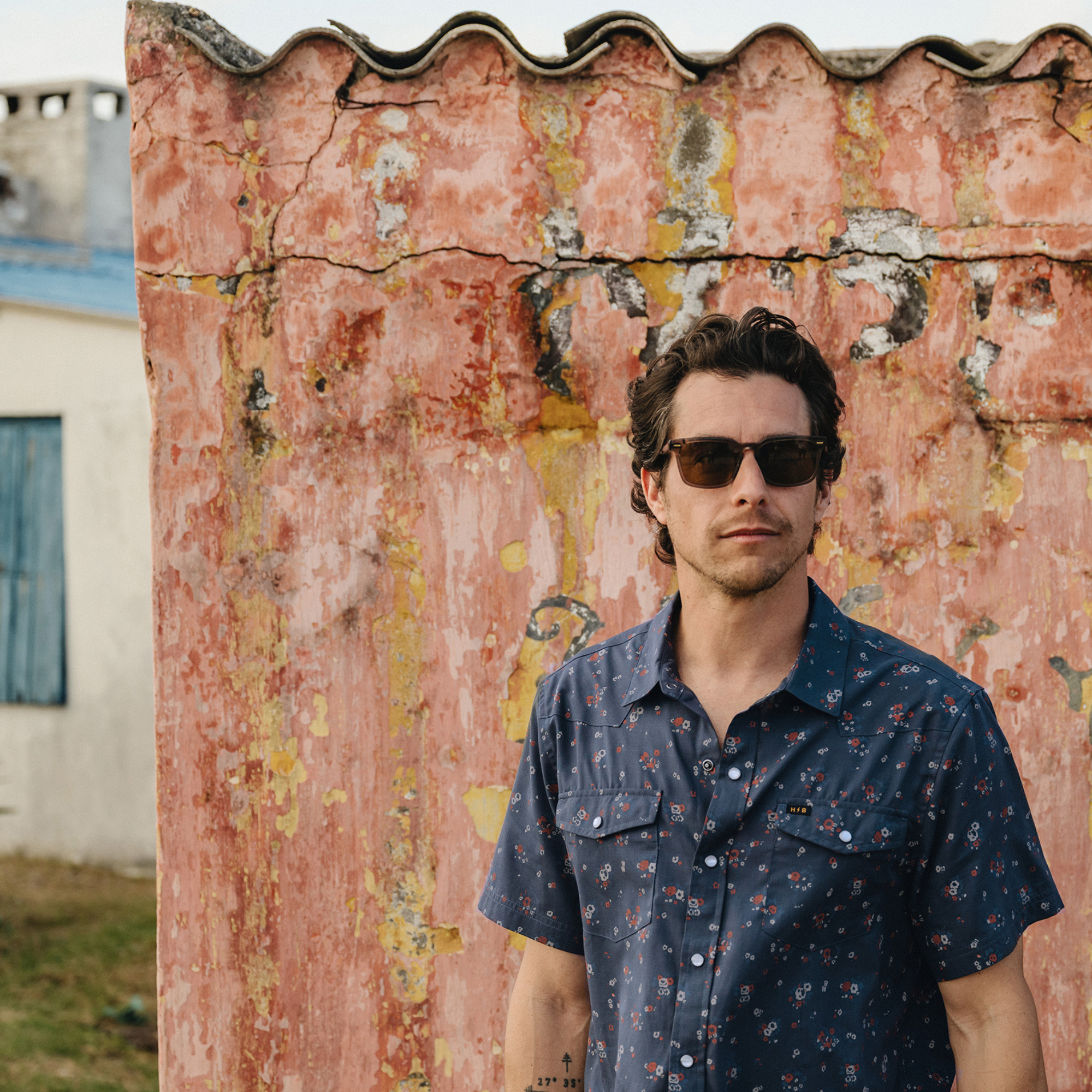a man in sunglasses wearing a Holwer Brothers H Bar B Snapshirt Bouquets in a midnight blue wiht small all-over floral print in an outdoor background