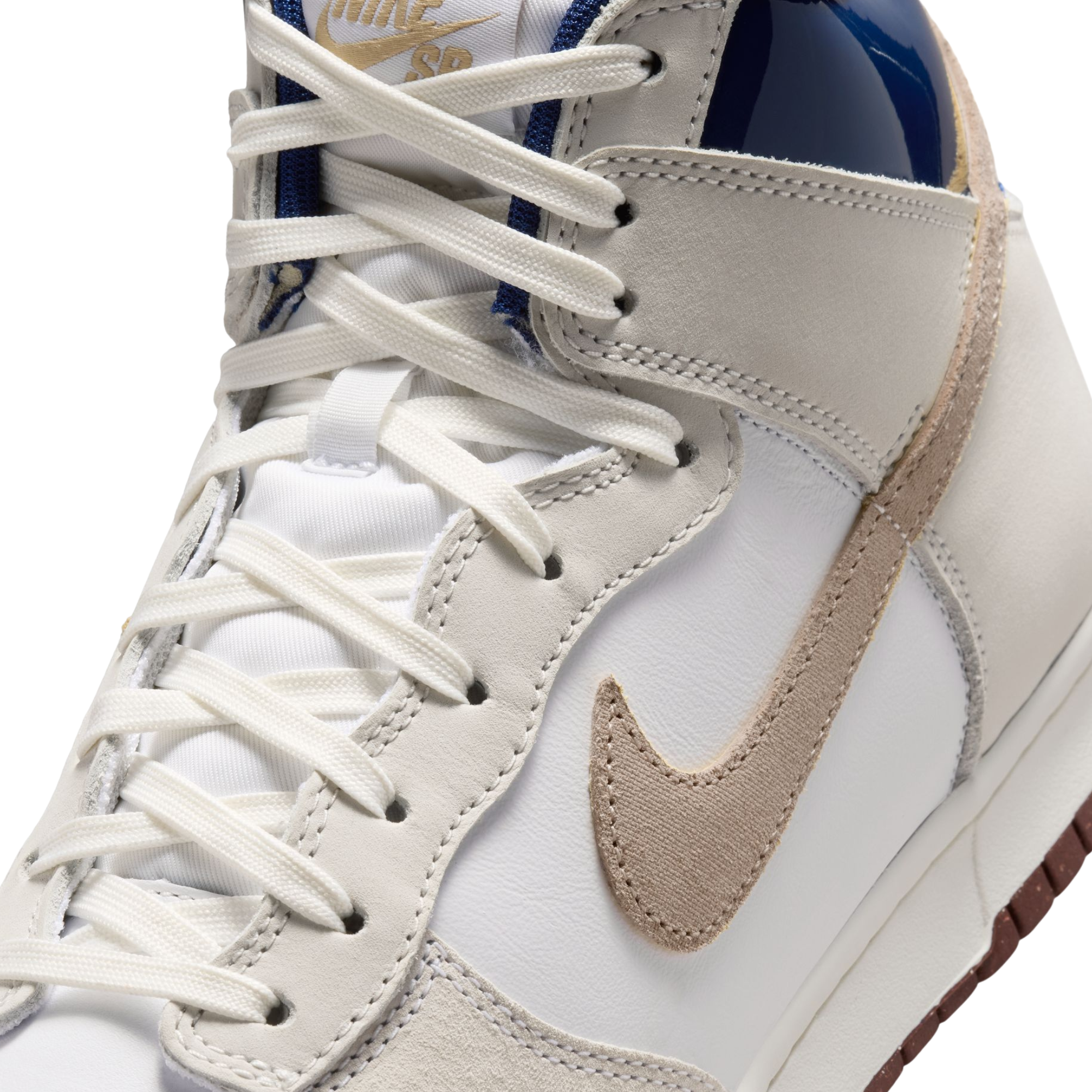 Close-up of a high-top Nike SB X Beyond Skate Shop sneaker in white leather with a beige Swoosh, white laces, a blue collar lining, and a gold Nike sb logo on the tongue.