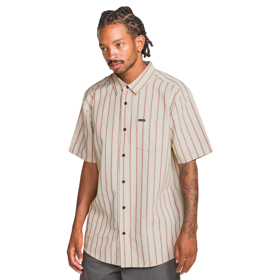 Man wearing a beige and red striped volcom sato stripe short sleeve shirt on a white background