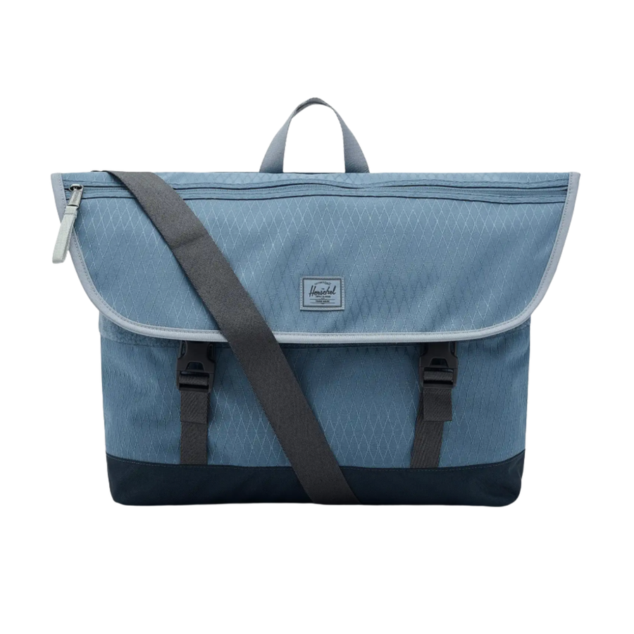 Blue herschel cove messenger bag with a black strap on a white background