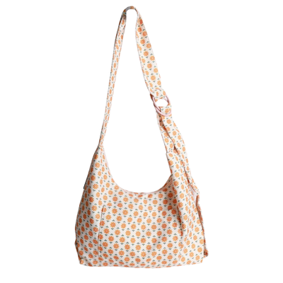 A slouchy thread shoulder bag with a white base and an all-over orange and yellow floral pattern, featuring a single adjustable shoulder strap.