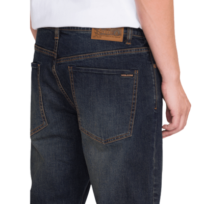 man in a white volcom logo t-shirt wearing dark blue volcom solver denim jeans with black converse all stars on a white background