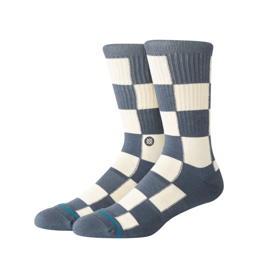 A pair of stance chaturanga crew socks with a blue-gray and cream checkerboard pattern, featuring a small circular Stance logo on the side and a thin teal stripe on the toes.