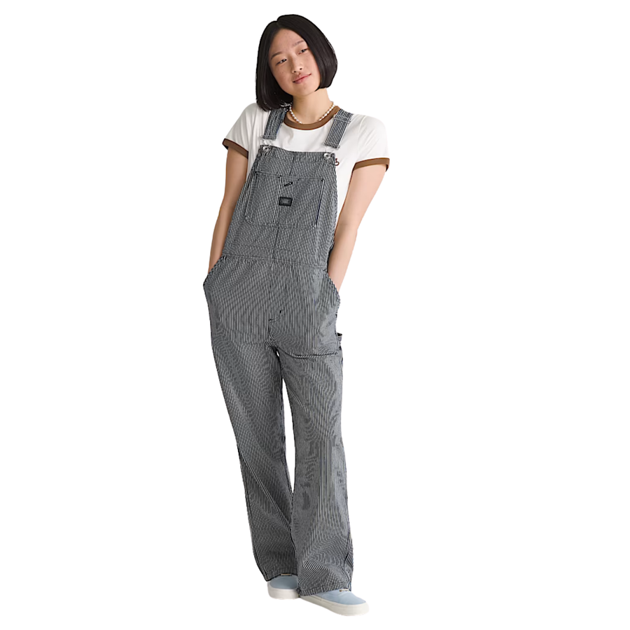 A woman modeling gray and white vans chore stripe vertically striped work overalls over a white t-shirt, standing against a plain white background.
