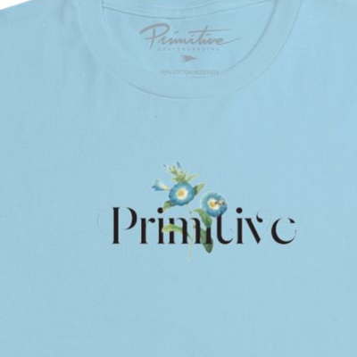A light blue short-sleeve crewneck t-shirt with a 'Primitive' logo printed on the chest, displayed flat against a solid white background.